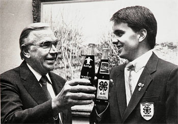 Donald R. Keough, president, The Coca-Cola Company, admires 4-H commemorative Coke bottle with Bill Gentry, state 4-H officer from Carroll County, Georgia. Keough is a member of National 4-H Council's Board of Trustees. (From 1985 Winter National 4-H Council Quarterly) 